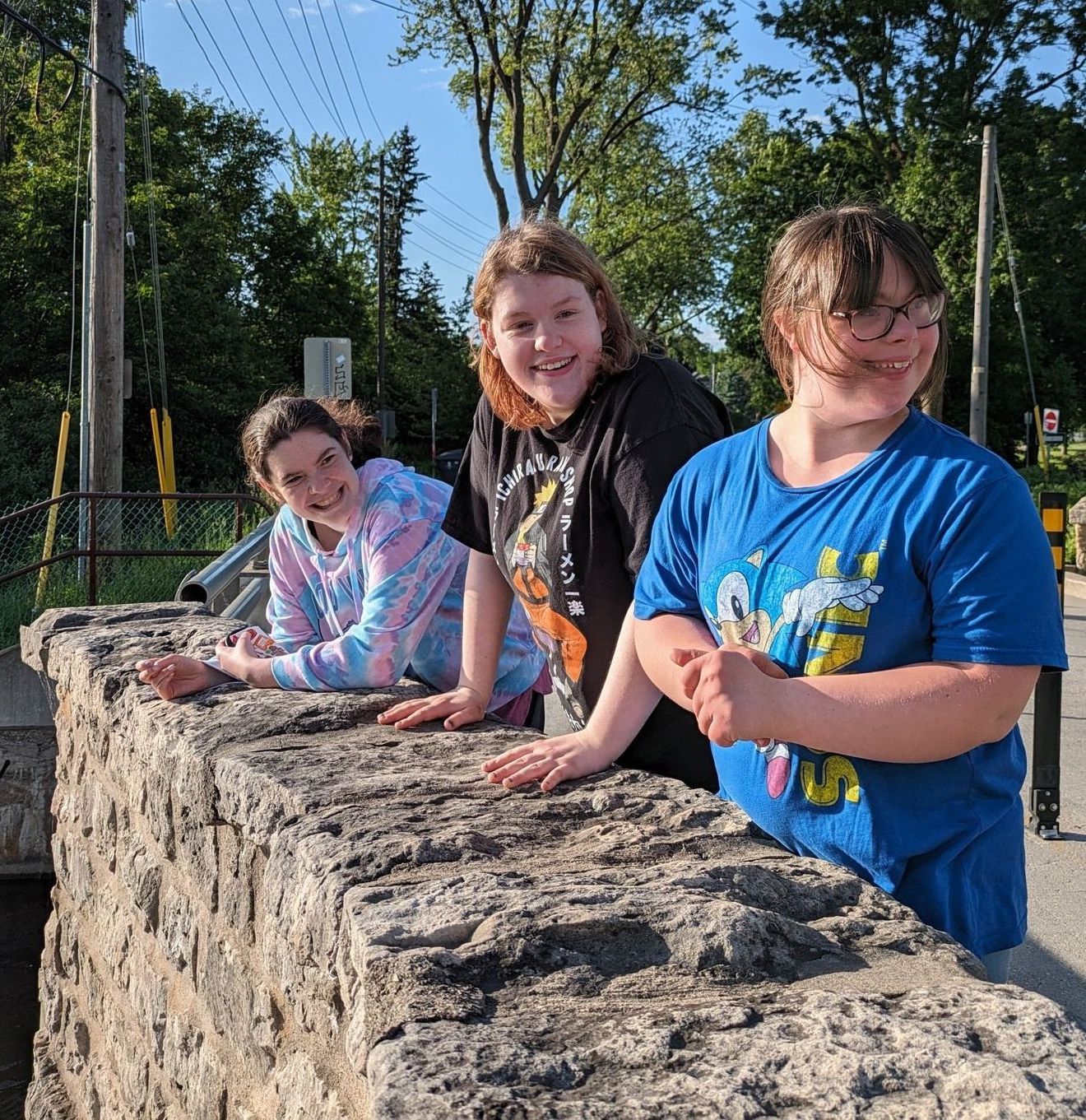 Three girls smiling on a stone bridge. 