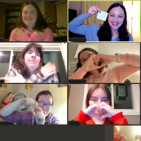 Six people in a video call; some make heart shapes with hands. One person holds a card.