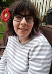Woman with glasses, flower in hair, wearing striped shirt, smiling outdoors.