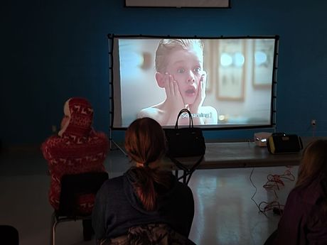 Women watching a movie projection screen; Macaulay Culkin on screen.