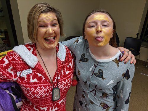 Two women in pajamas with gold face masks, making silly faces.