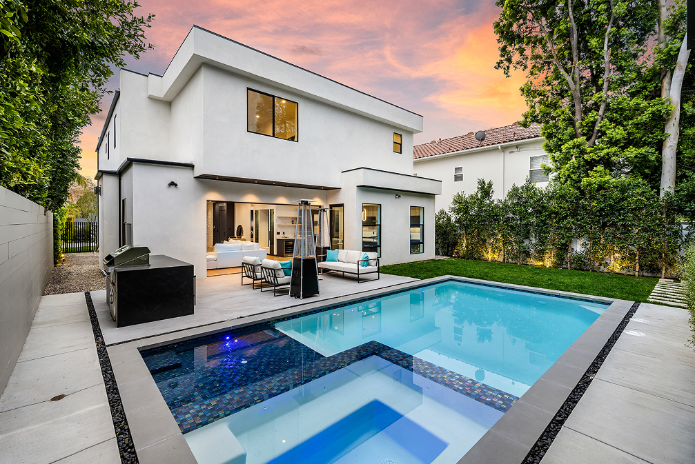 Modern white house with a pool and jacuzzi in a backyard at sunset.