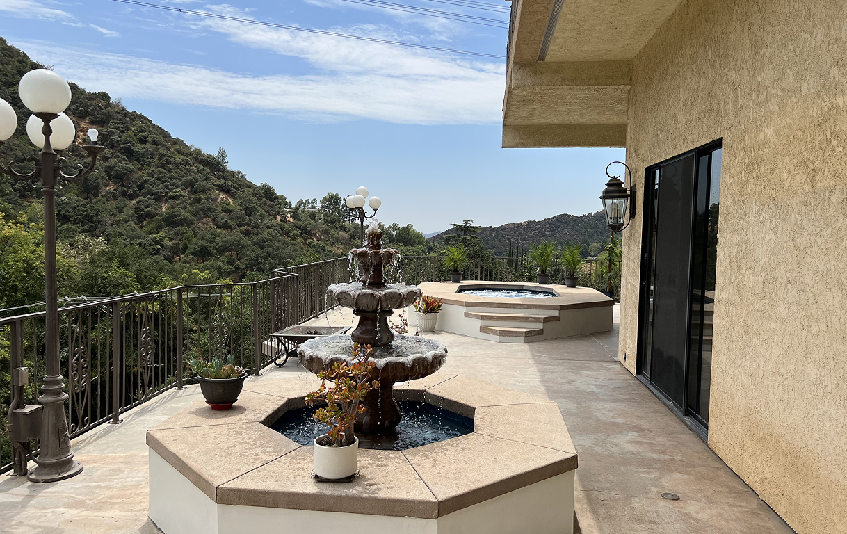 Patio with tiered fountain, hot tub, and view of mountains under a blue sky.