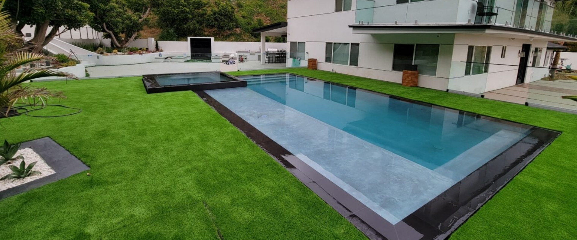 Modern backyard with a rectangular swimming pool, green lawn, and patio beside a white house