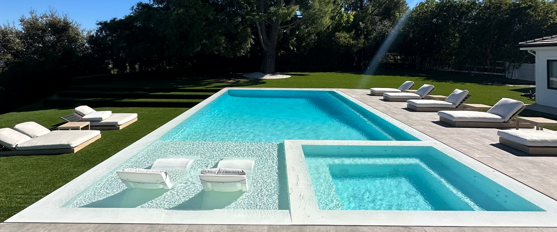 Swimming pool with white deck and furniture in an outdoor setting.