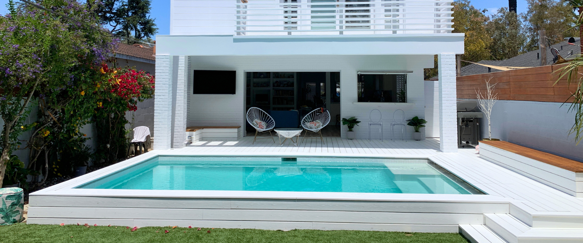 Swimming pool with white deck and furniture in an outdoor setting.