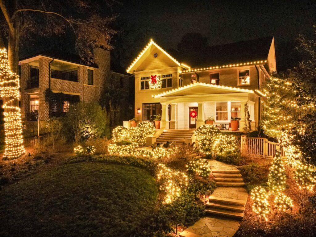 Christmas-lit house at night with glowing string lights, warm porch, and winding stone steps through a landscaped yard