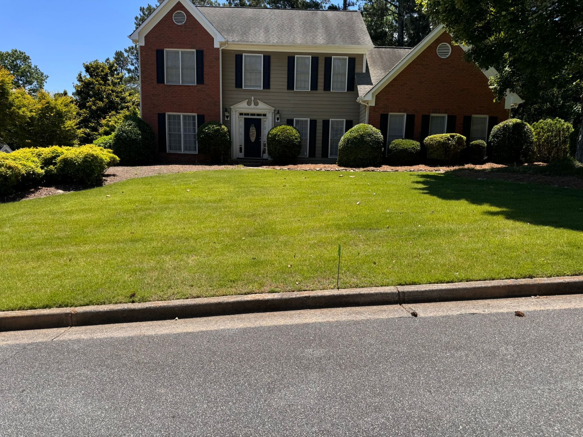 Suburban two-story brick house with a large green lawn and trees in front