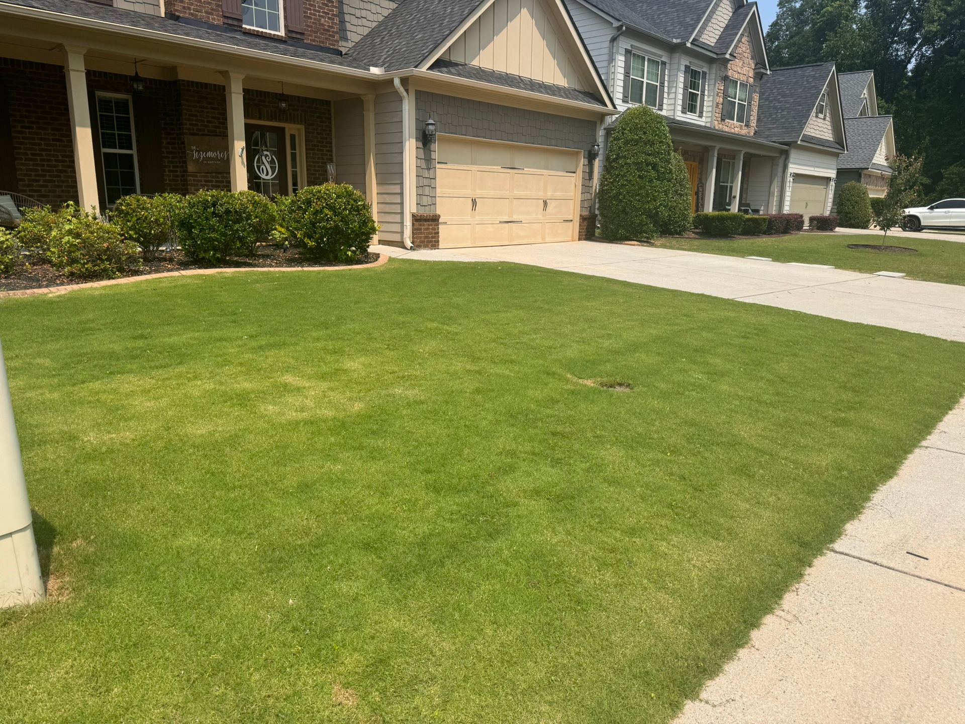 Suburban house with a green front lawn, driveway, and sidewalk on a sunny day