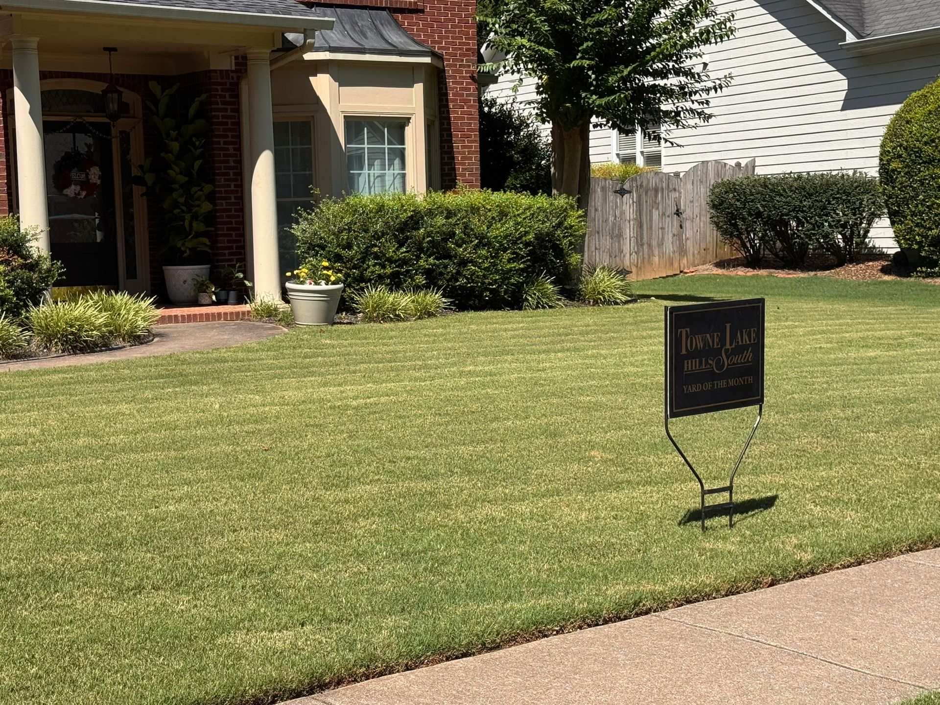 Suburban lawn with a small black yard sign near a sidewalk and a house in the background