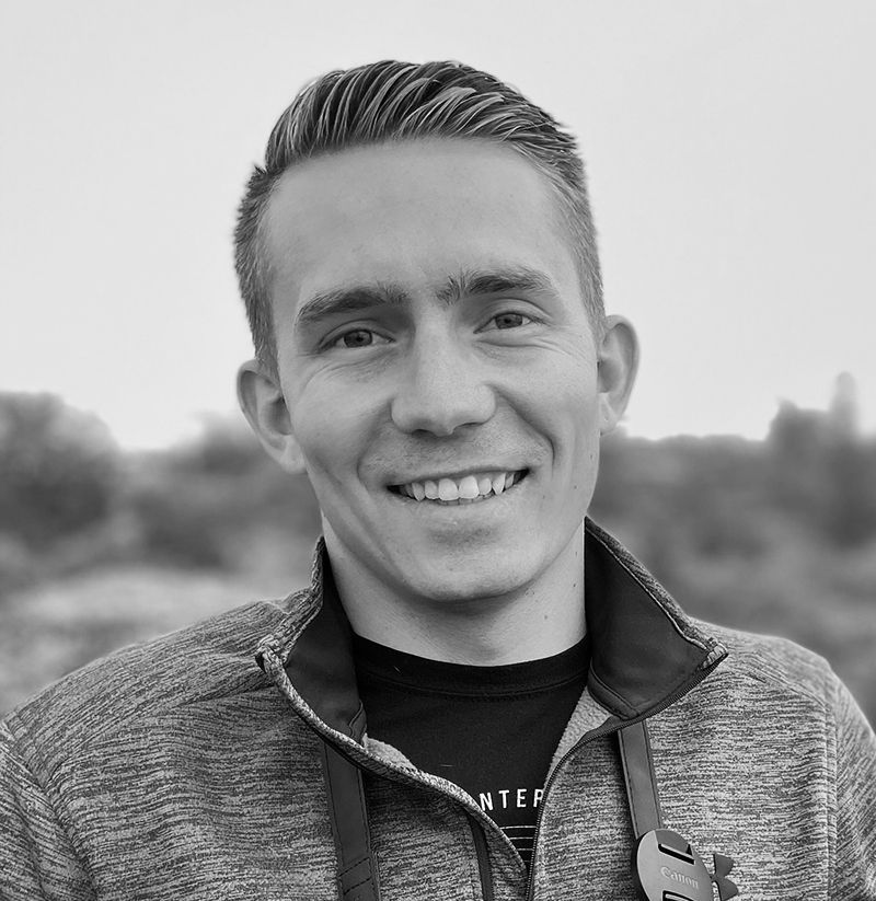 Smiling man in a grey jacket, posing outdoors.