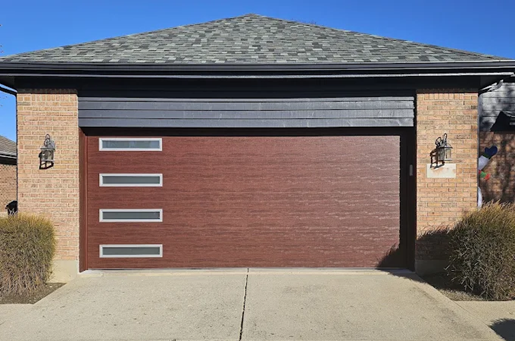 Brown garage door with windows, brick facade, and shrubs.