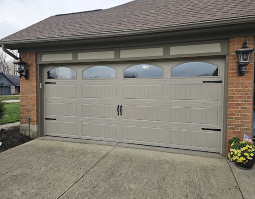 Tan garage door with arched windows and black hardware on brick house.