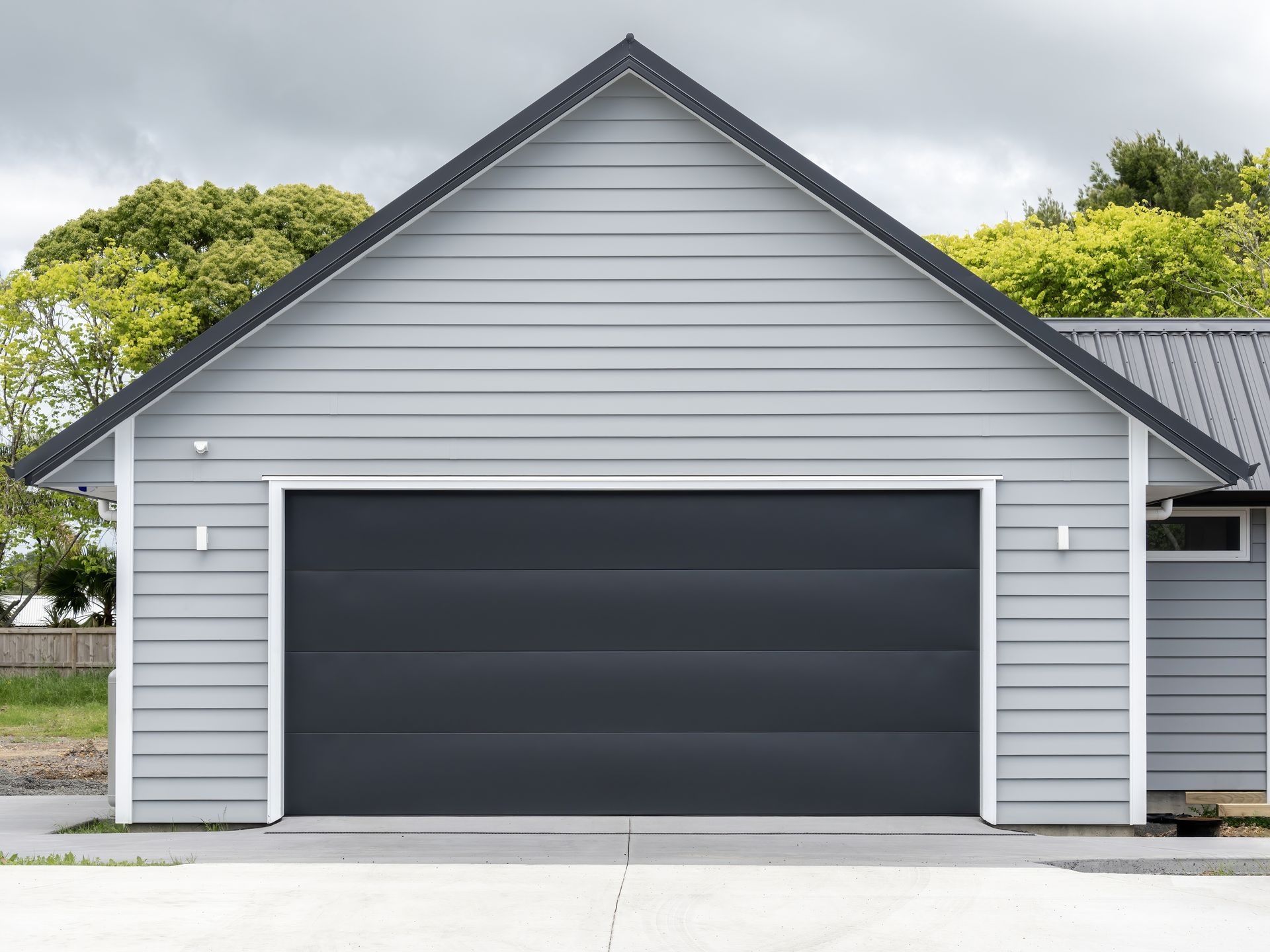 Typical double detached gray garage with black tilt-up raised-panel retractable metal door.