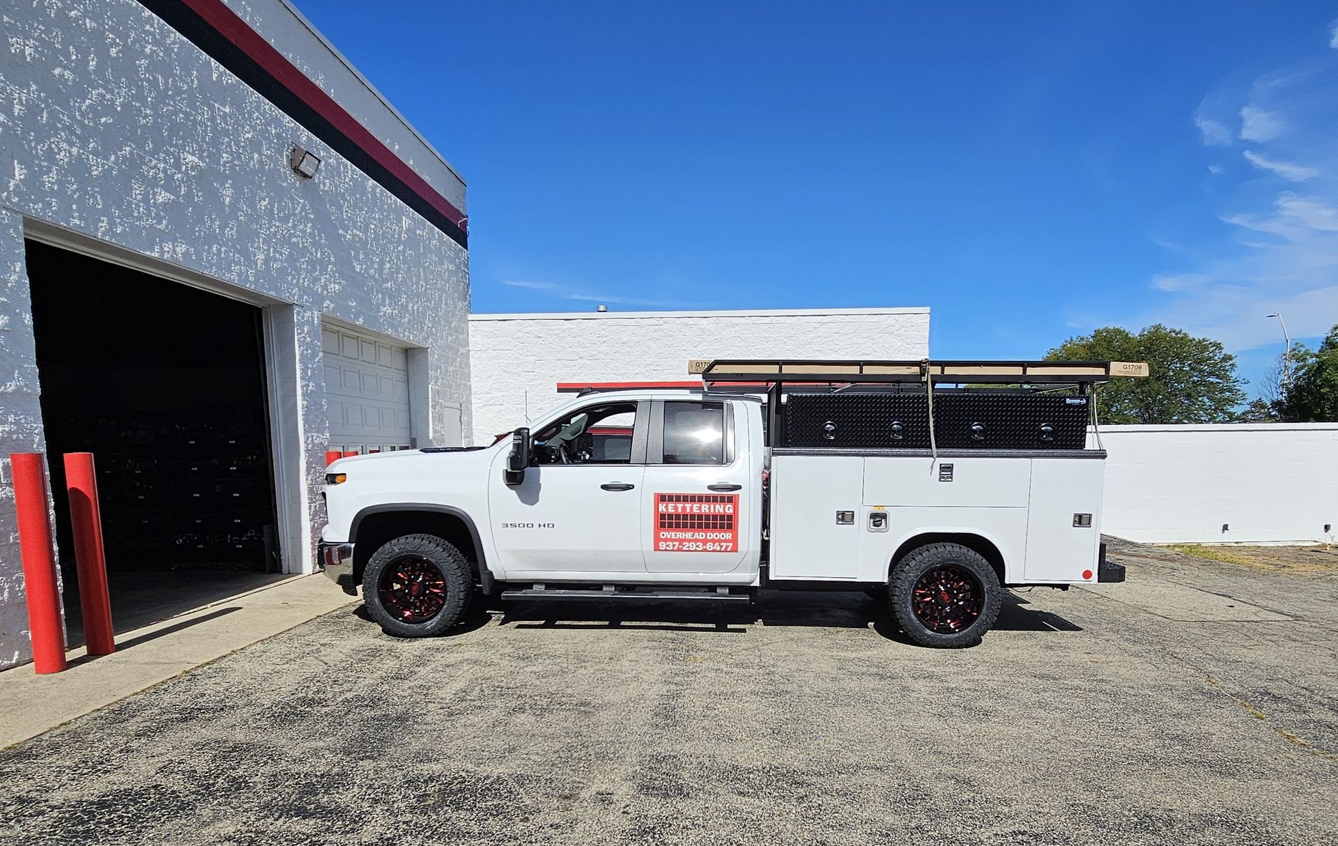 White work truck with tool boxes parked next to a building on a gravel lot under a blue sky.