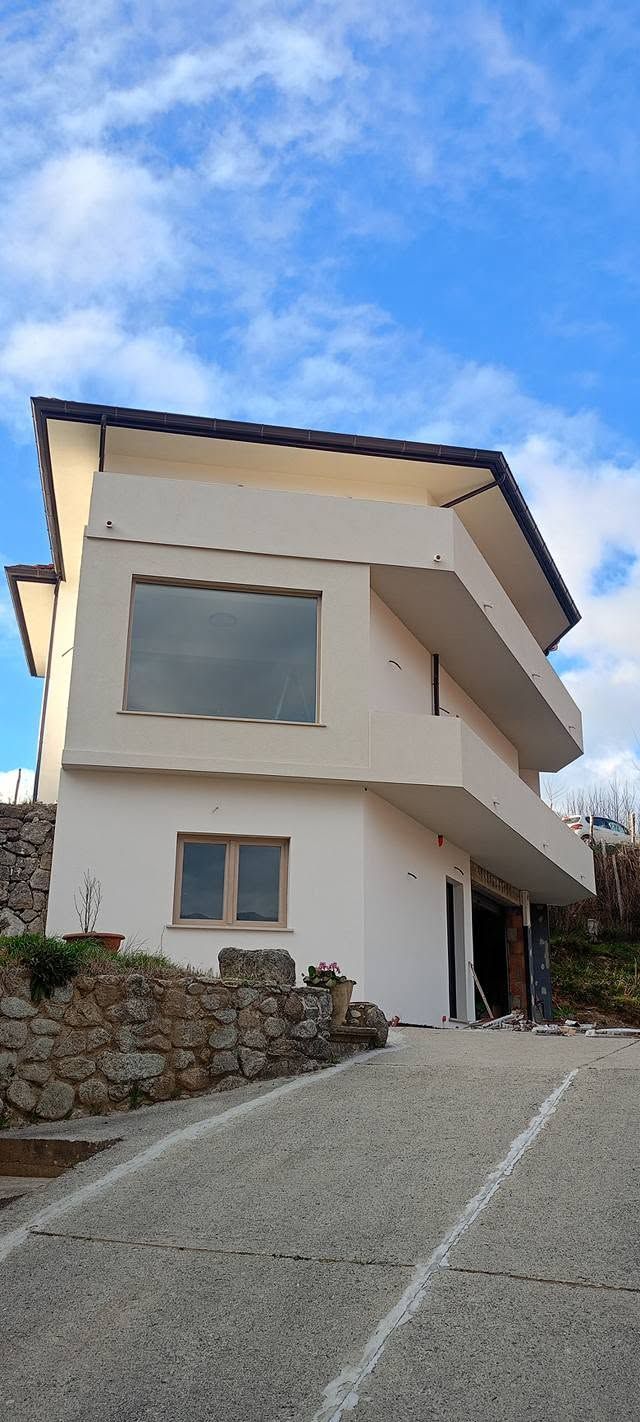 Casa moderna bianca con grandi finestre su un ripido vialetto sotto un cielo azzurro