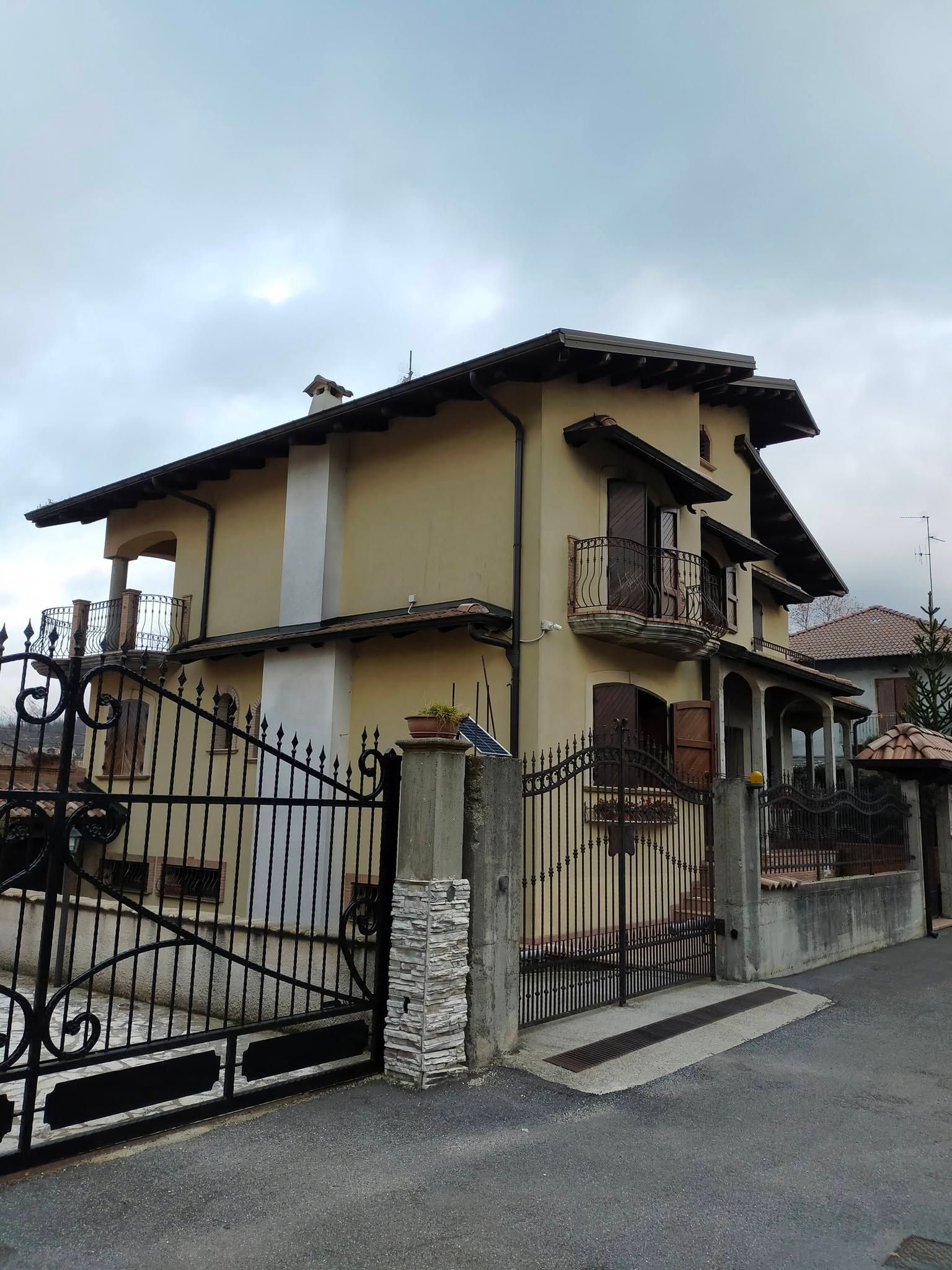 Casa beige a due piani con cancello e recinzione in ferro battuto, situata in una strada tranquilla.