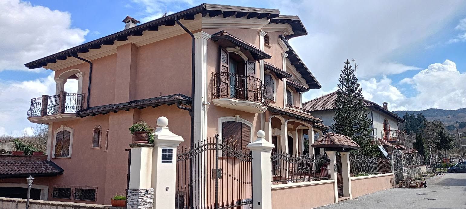 Casa a due piani color pesca con balconi in ferro battuto e ingresso con cancello sotto un cielo azzurro