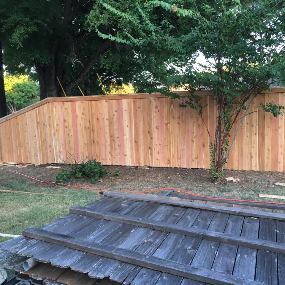 Wooden fence in a yard, under trees. Old wooden planks in foreground.