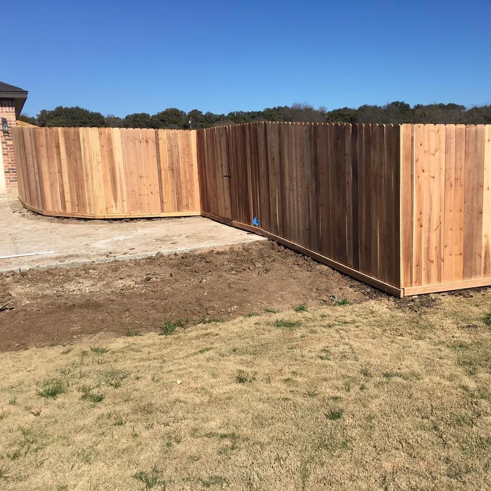 Wooden fence around a patio, set in a yard with brown grass and blue sky.