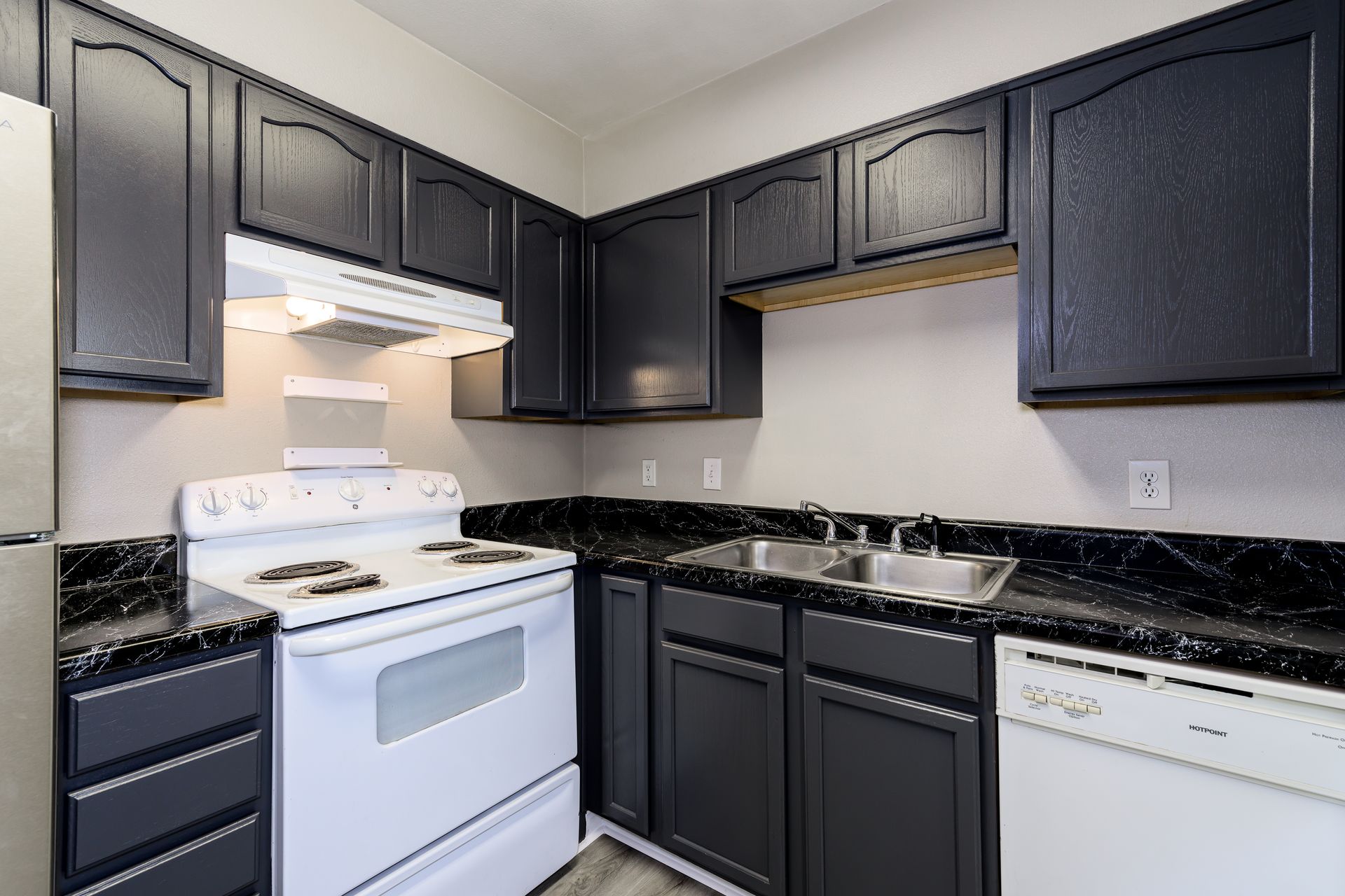 A kitchen with black cabinets , white appliances , and a sink.