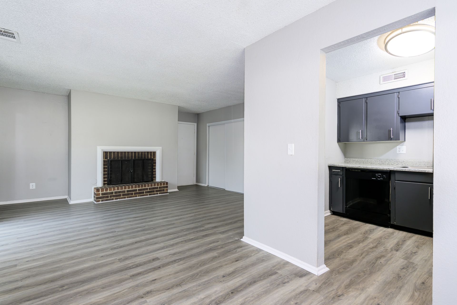 An empty living room with a fireplace and a kitchen.