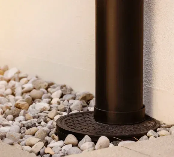Brown downspout pipe on a gravel bed beside a beige wall
