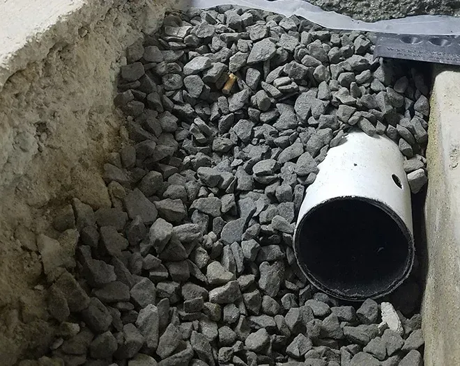 Gray gravel in a trench with a white PVC pipe section lying on its side