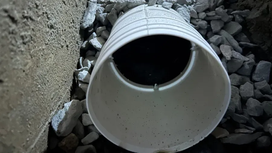 Large white PVC pipe opening surrounded by gravel in a trench