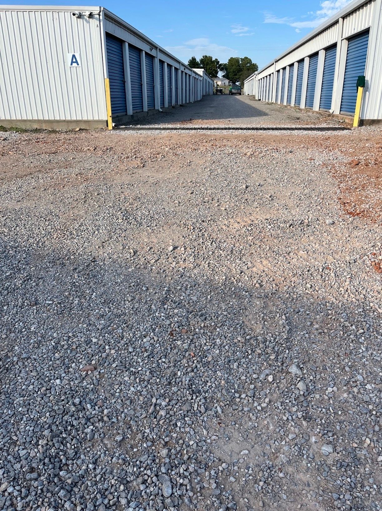Gravel driveway between rows of white storage units under a blue sky