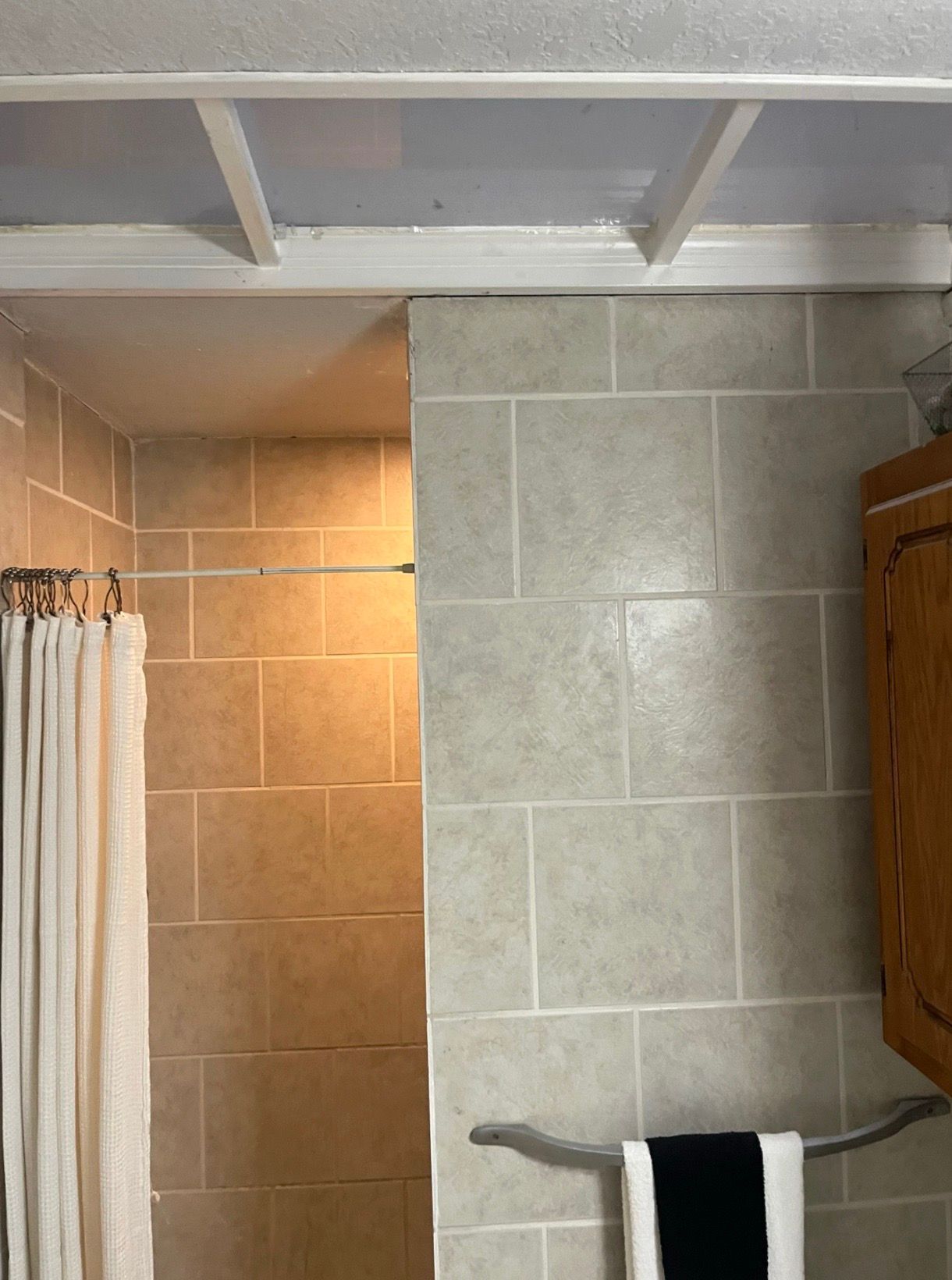 Bathroom with beige tiled shower, white curtain, and towel bar beneath exposed ceiling beams.