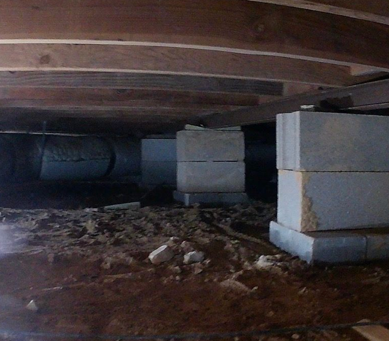 Crawlspace under a wooden floor with stacked cinder blocks and dirt ground.