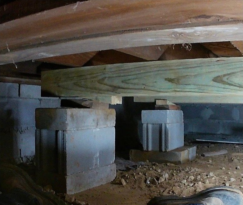 Crawlspace with wooden beams supported by concrete blocks and dirt floor under a house