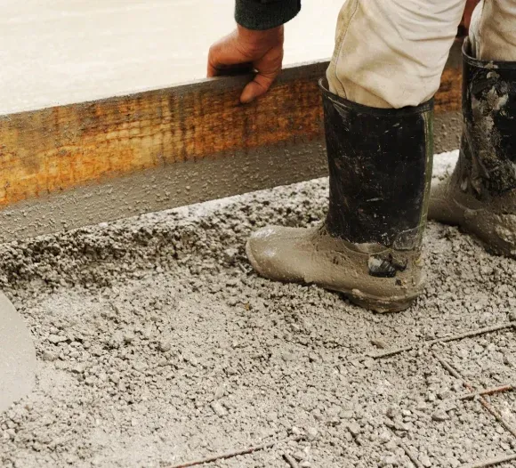 Worker in black boots smoothing wet concrete on a floor beside a wall