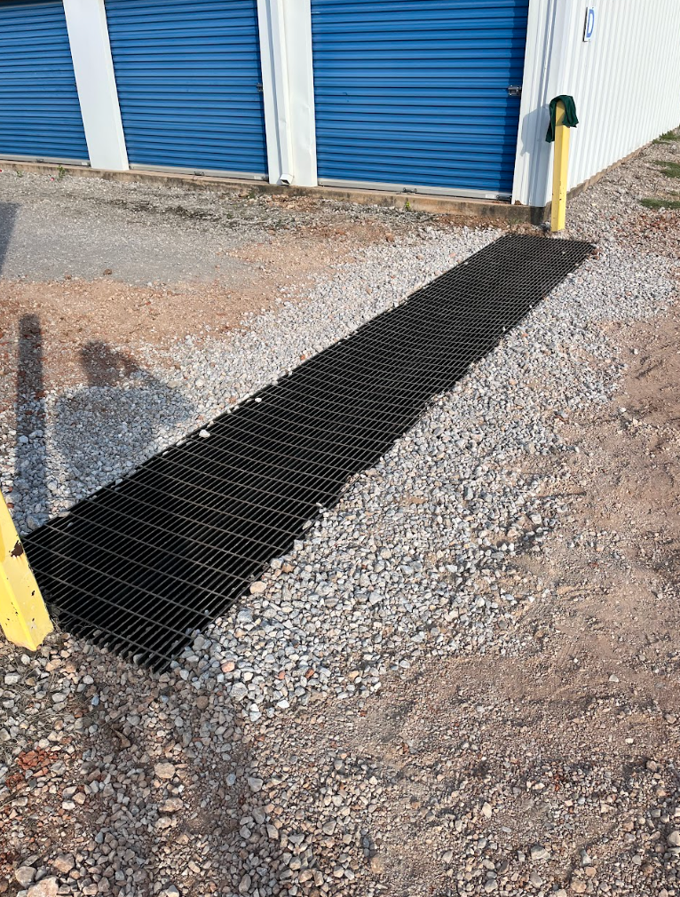 Black metal mat leading to blue storage unit doors over gravel.