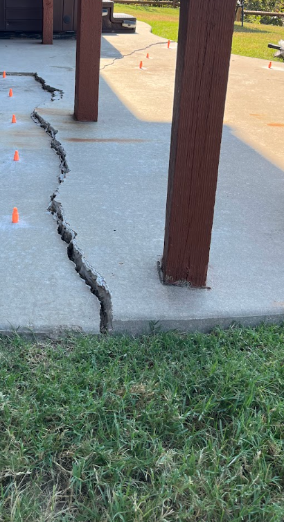 Cracked concrete patio beside wooden posts, with orange cones marking the damaged area.