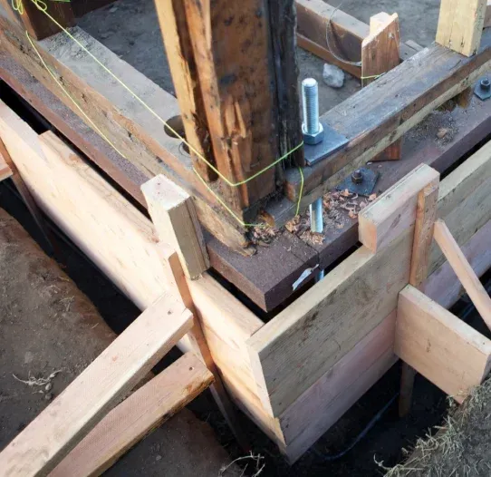 Wooden formwork around a concrete foundation corner with anchor bolts and braces.