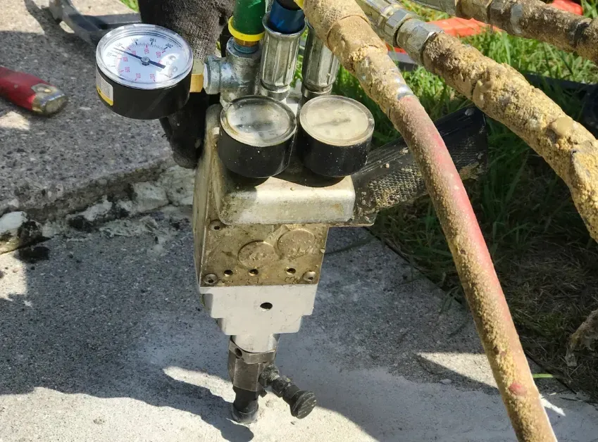Outdoor utility meter with four dials, mounted beside a wet concrete walkway and garden hose.