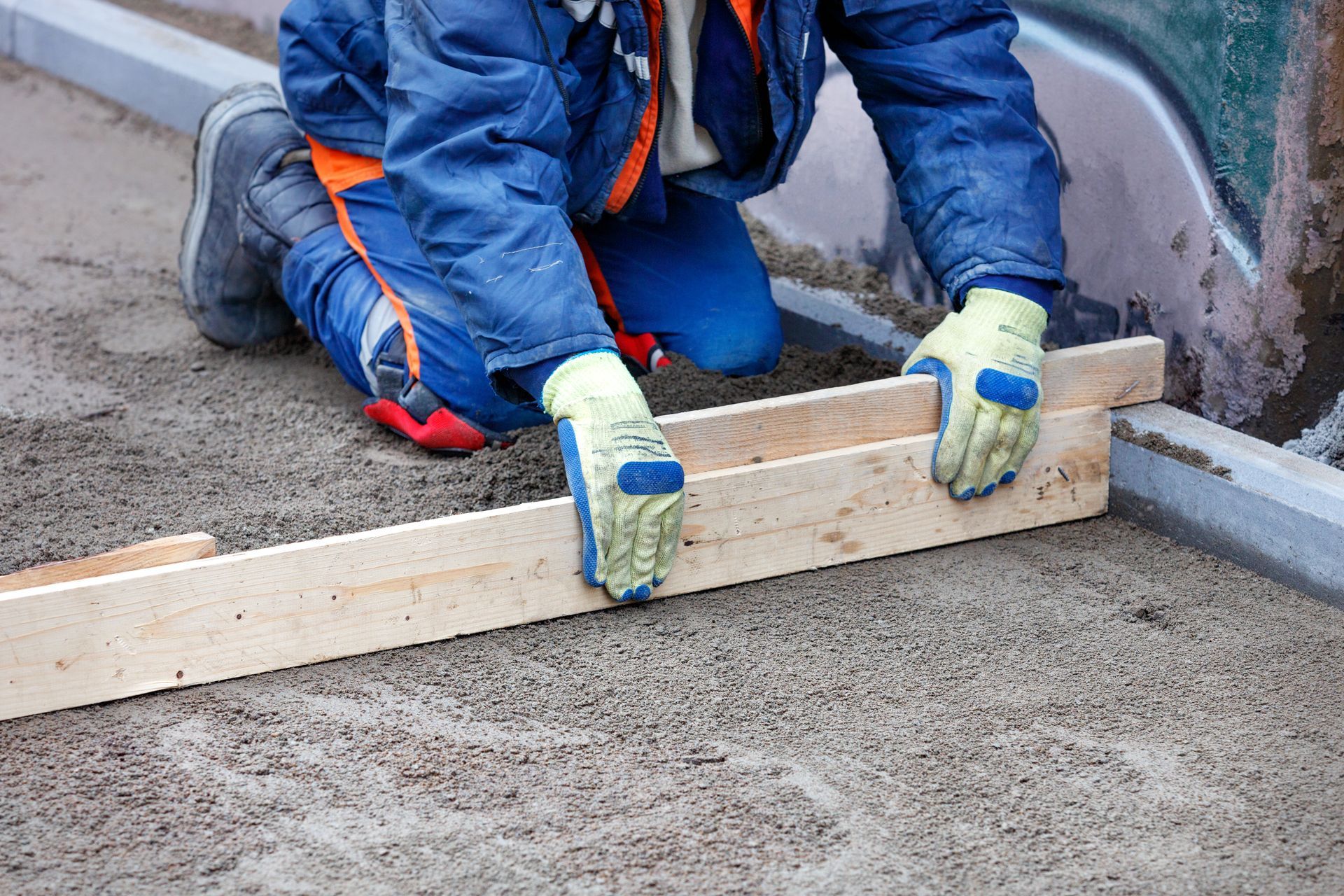 Worker leveling wet concrete with a straight board at a construction site