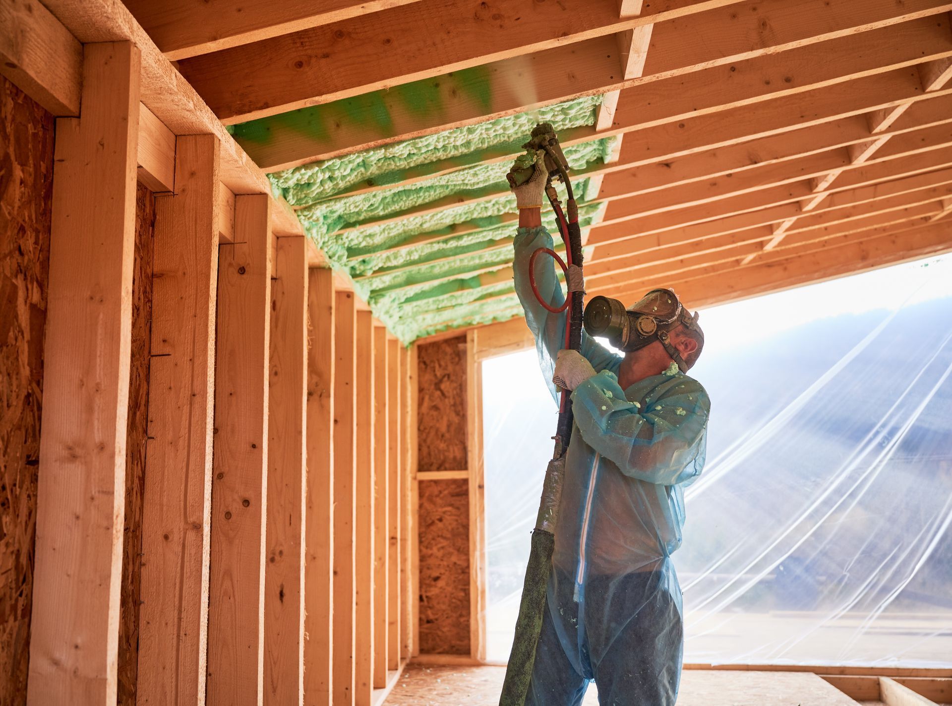 Worker insulating a ceiling cavity in a wooden-framed room with a spray hose