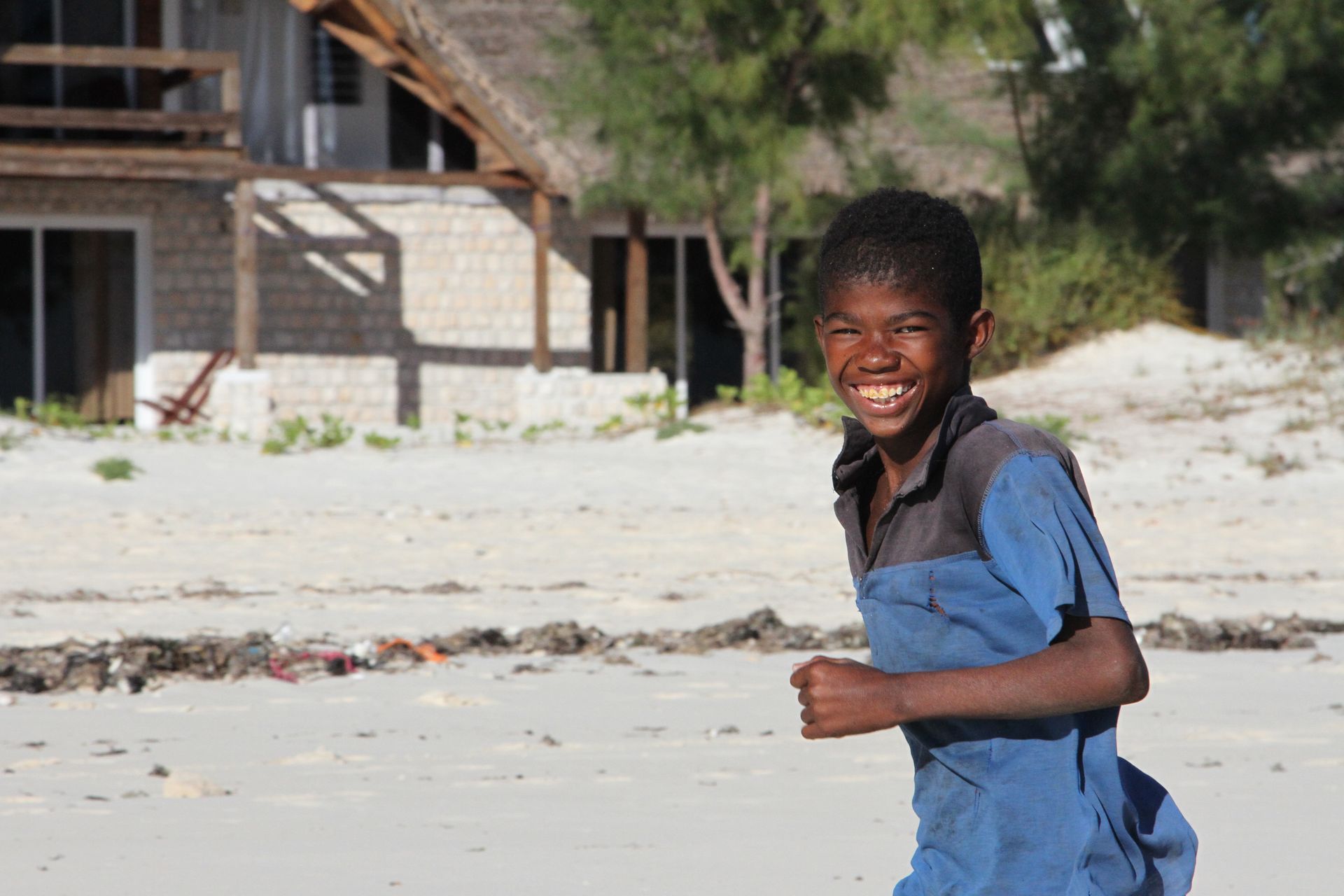 Smiling child running on a sandy beach near a wooden building