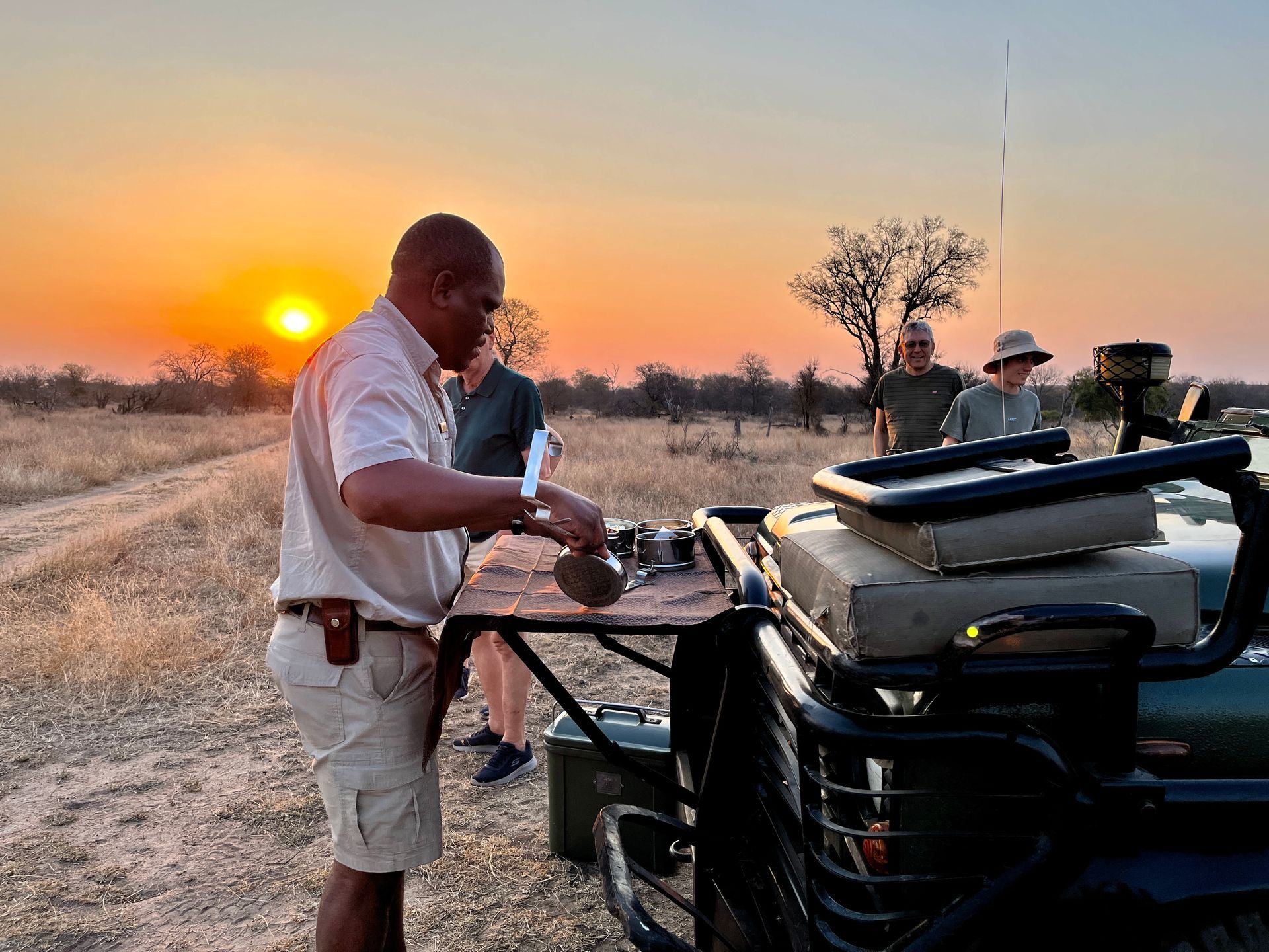 Man grilling at sunset beside an off-road vehicle in a dry field