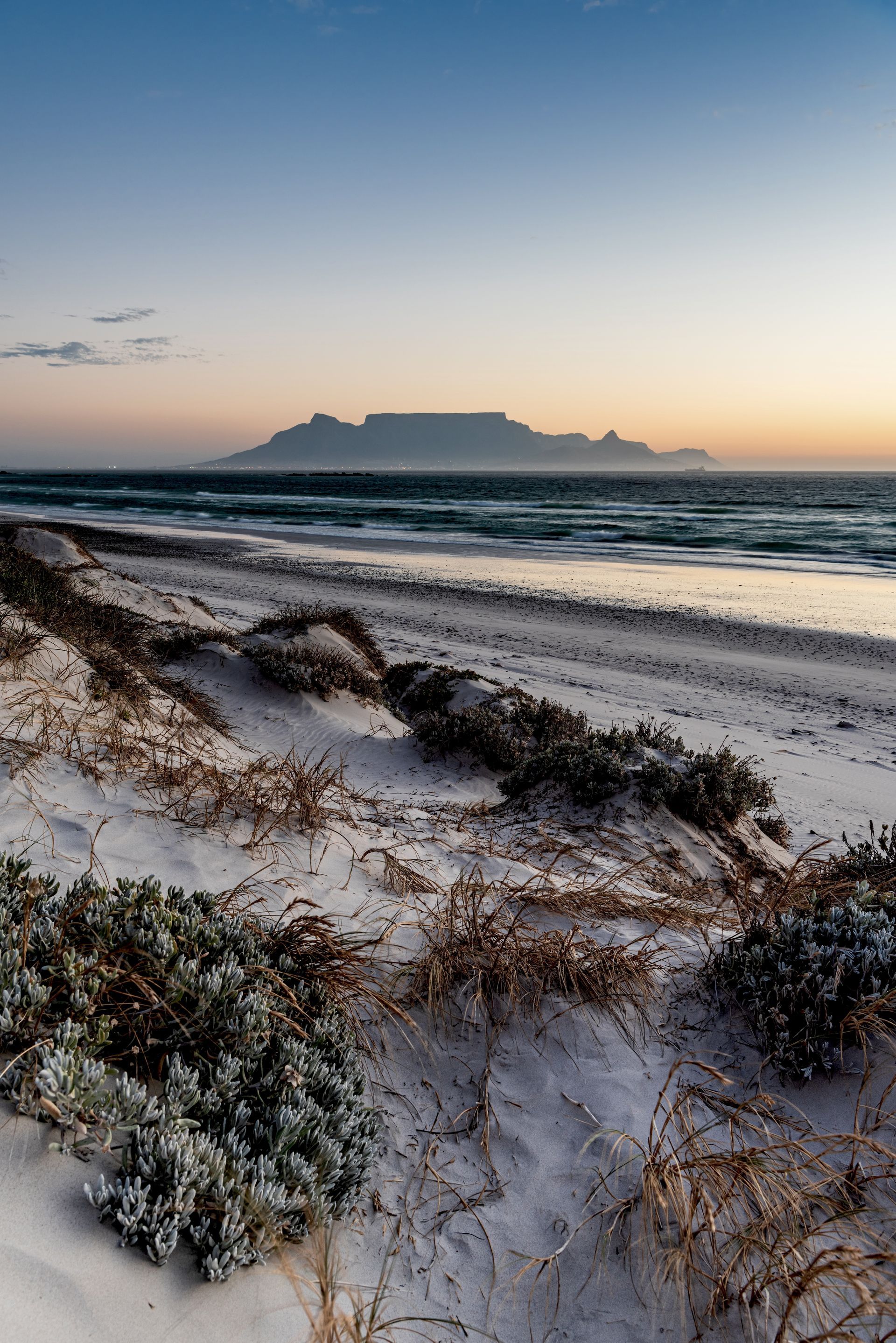 Sunset over a sandy beach with waves and a distant flat-topped island on the horizon