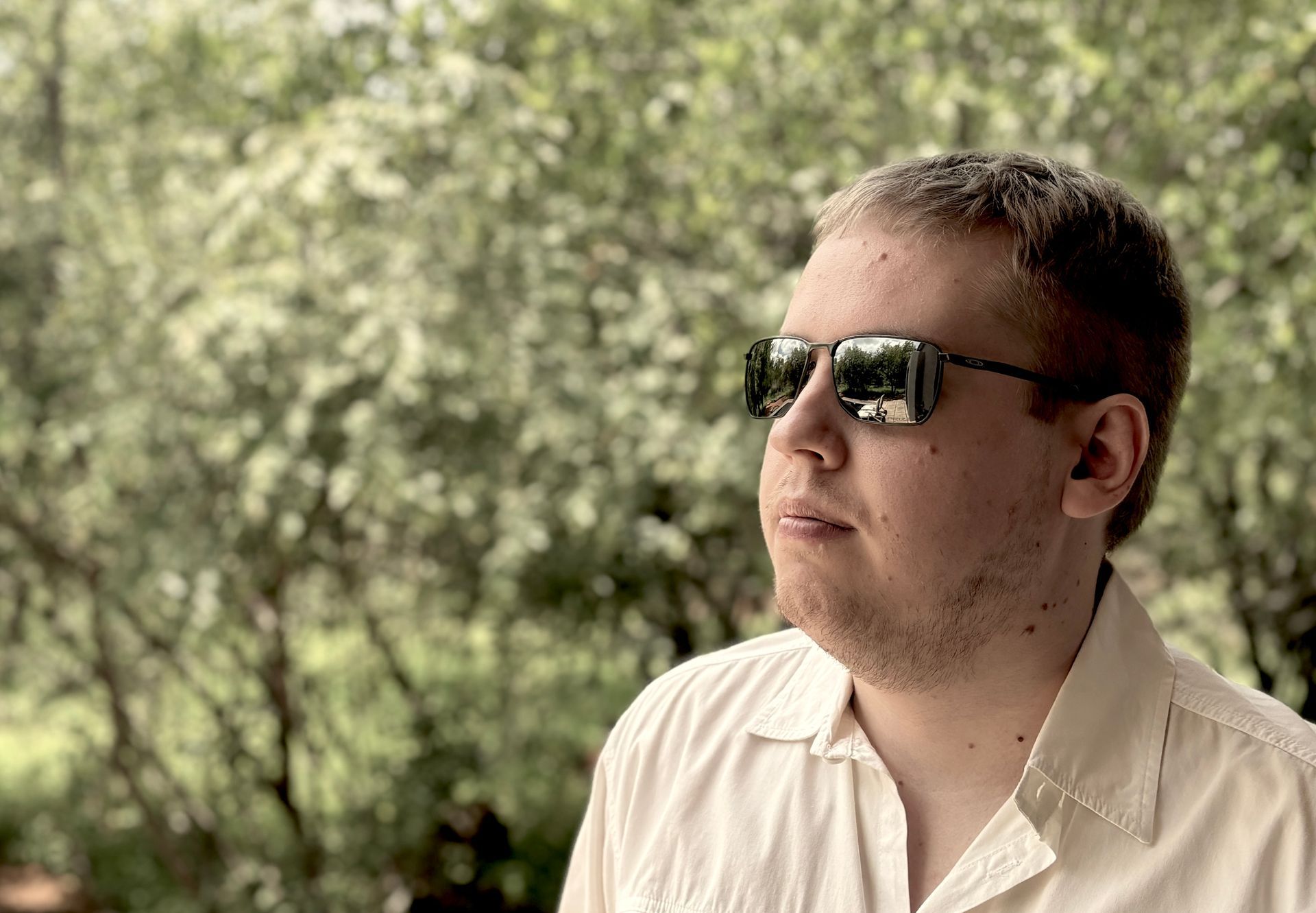 Person in sunglasses standing outdoors against a blurred green background.