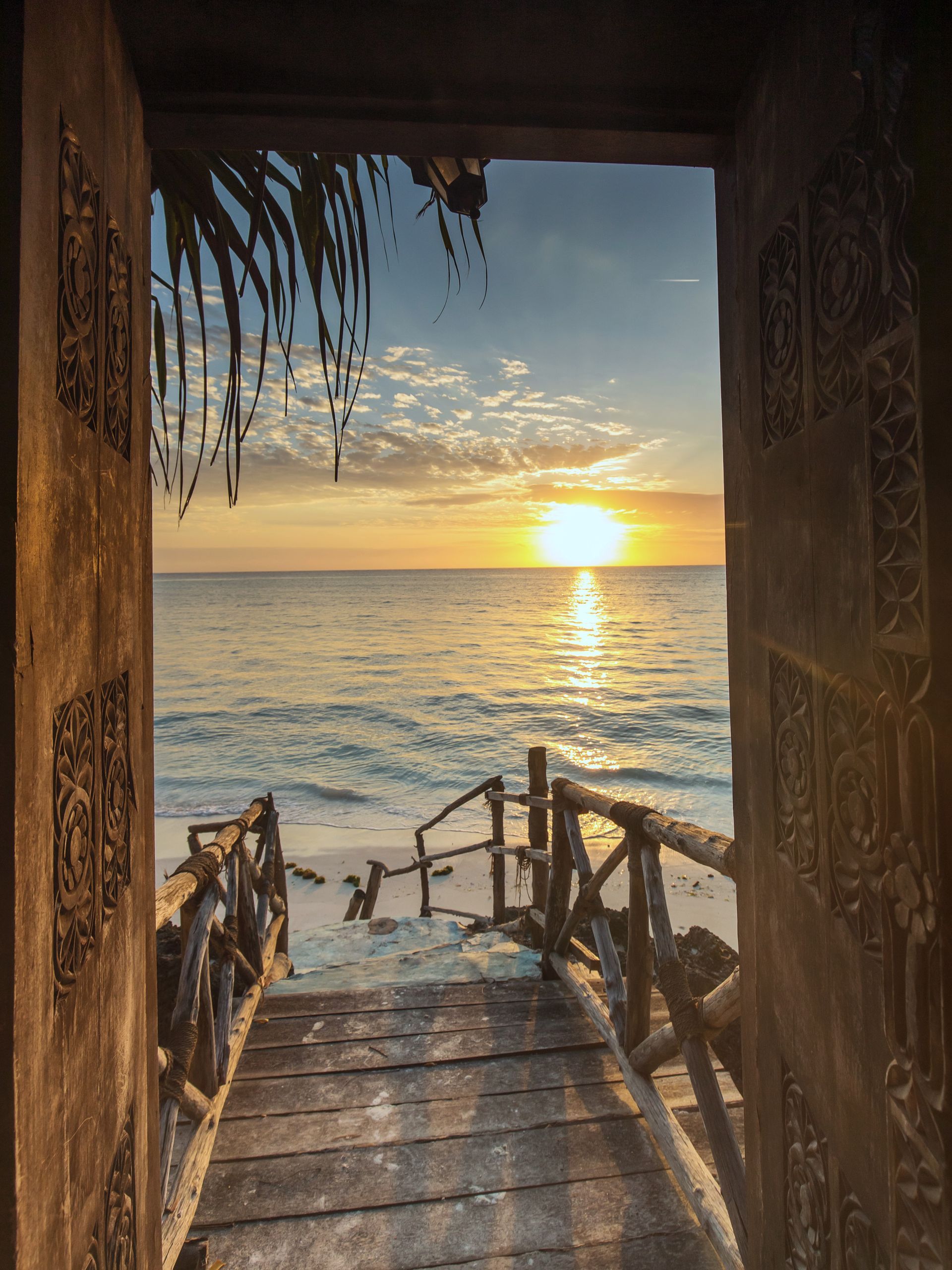 Sunset over the ocean framed by a wooden doorway and thatched porch steps