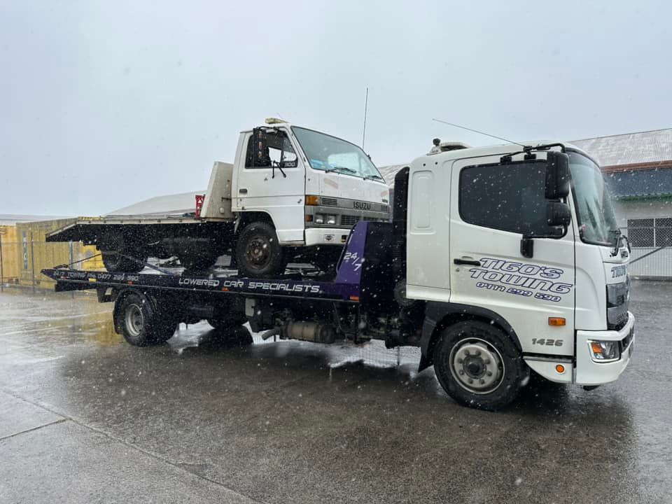 White Tow Truck With Small White Truck on Its Flatbed in Snowy Conditions — Tigo’s Towing In Cairns City, QLD