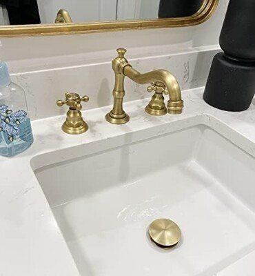 Gold faucet and sink in a bathroom. White countertop, gold mirror, and black decorative items.