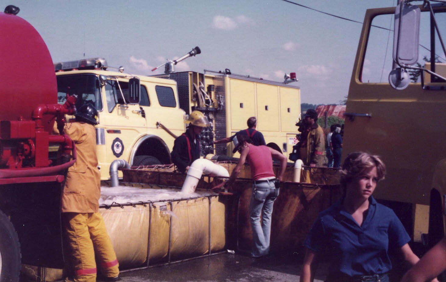People spraying water on a yellow fire truck at a roadside scene