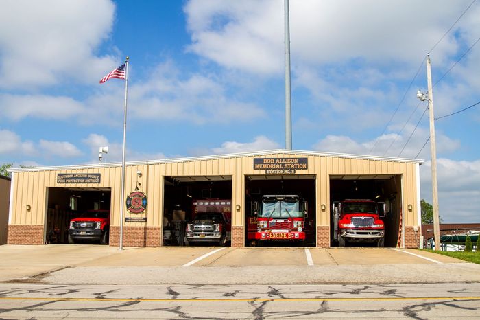 Fire station with open garage bays and fire trucks parked inside under a blue sky