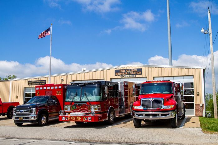 Fire station with two red fire trucks and a black SUV parked in front under a blue sky
